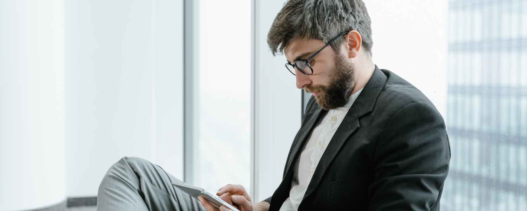 bearded man in black suit jacket using a tablet